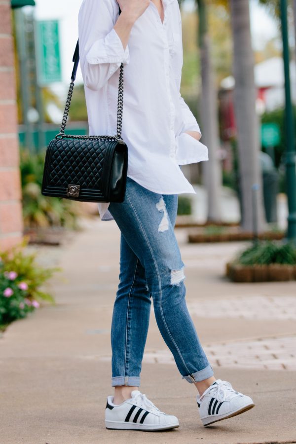 https://faviana.com/cdn/shop/articles/AG-Jeans-Stilt-Crop-roll-up-jean-17-year-riot-Adidas-Superstar-sneaker-Chanel-boy-bag-white-button-down-shirt-with-distressed-denim-outfit-600x900.jpg?v=1639655785