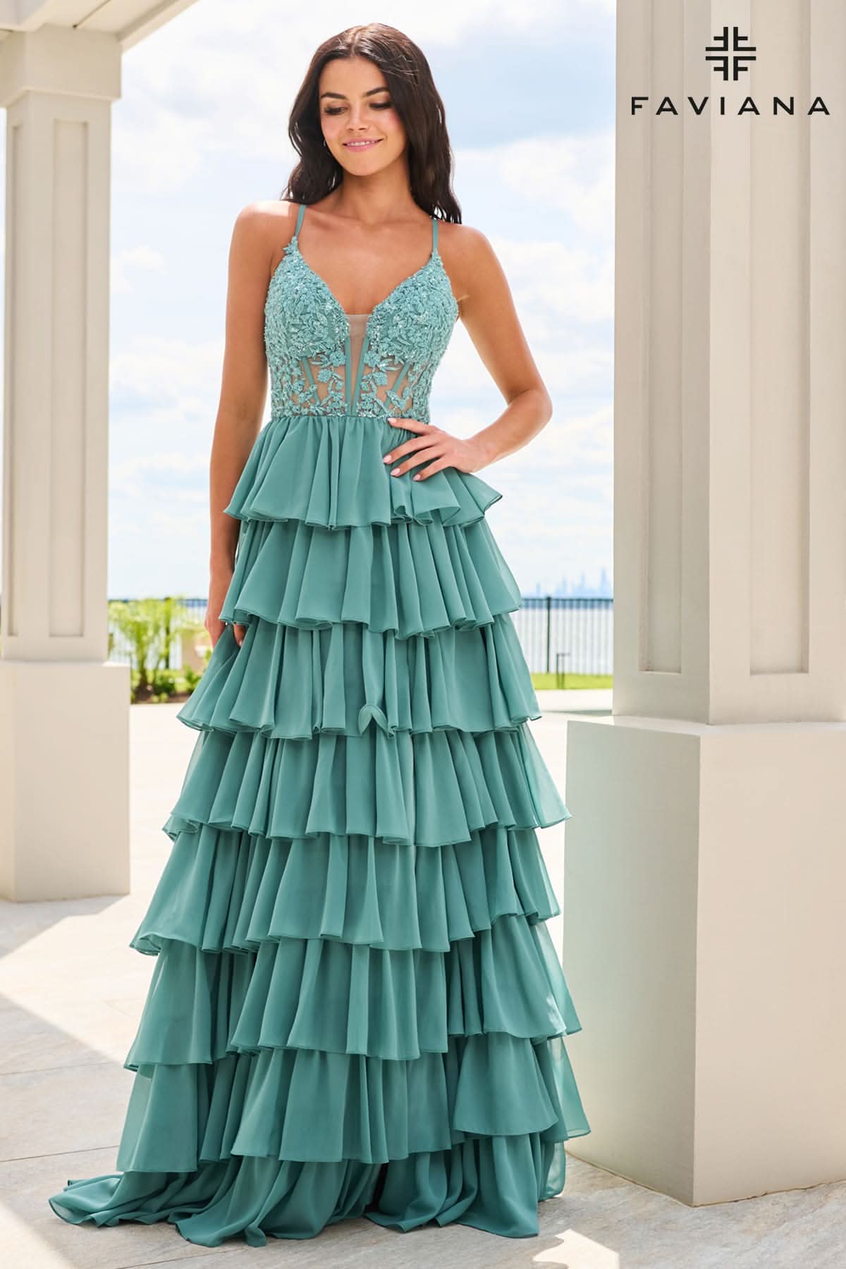 A woman models a teal green formal gown with a lace bodice and a tiered ruffle skirt, standing in a sunny outdoor setting with white columns. The brand name 'FAVIANA' is visible in the top right corner.