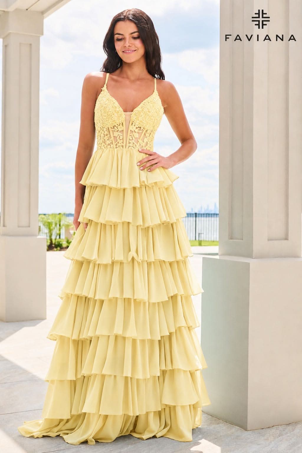 A woman models a yellow sleeveless maxi dress with a lace bodice and a tiered ruffle skirt, standing in front of a white colonnade. The FAVIANA brand logo is visible in the top right corner.